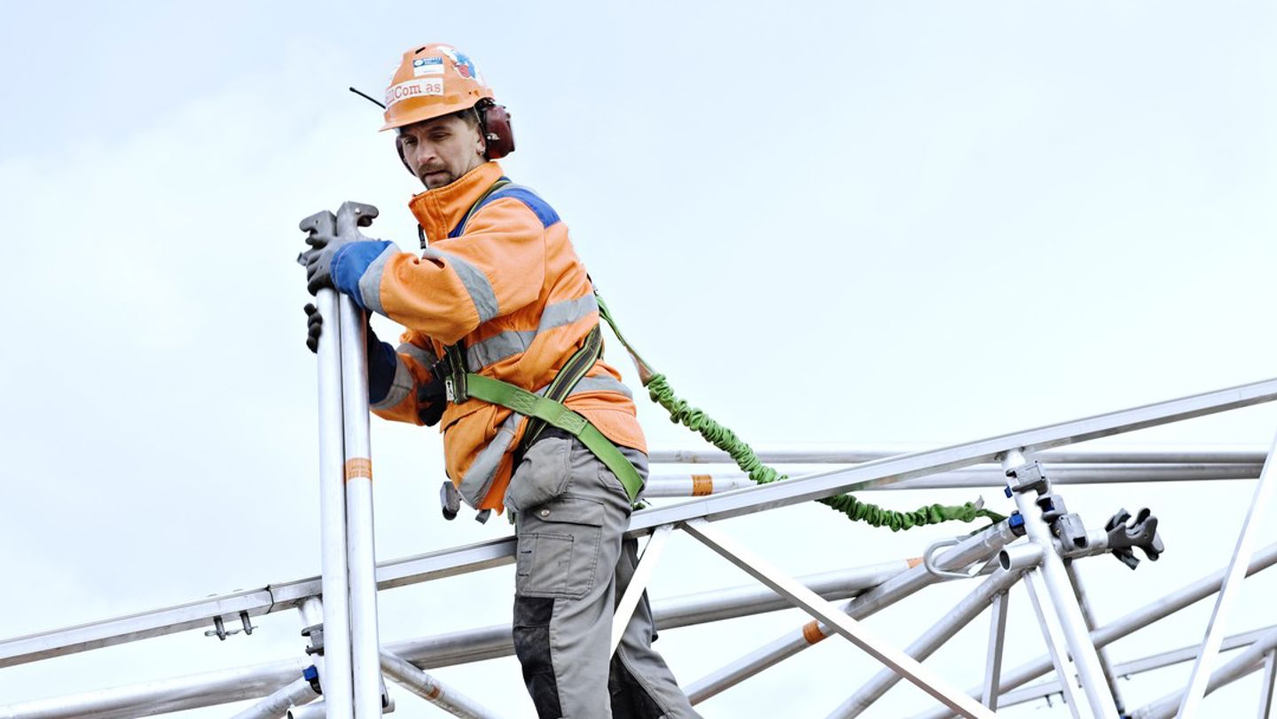 Arbeidstakar med verneutstyr monterer stillas i høgda.
