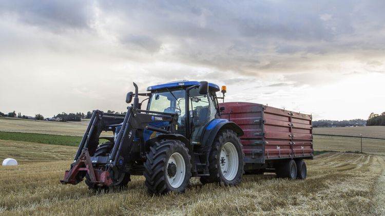 Bilde av en blå traktor på en åker.