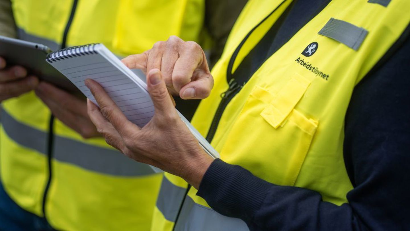Bildet viser hendene til to inspektører som har på seg gul Arbeidstilsynet-vest. 
