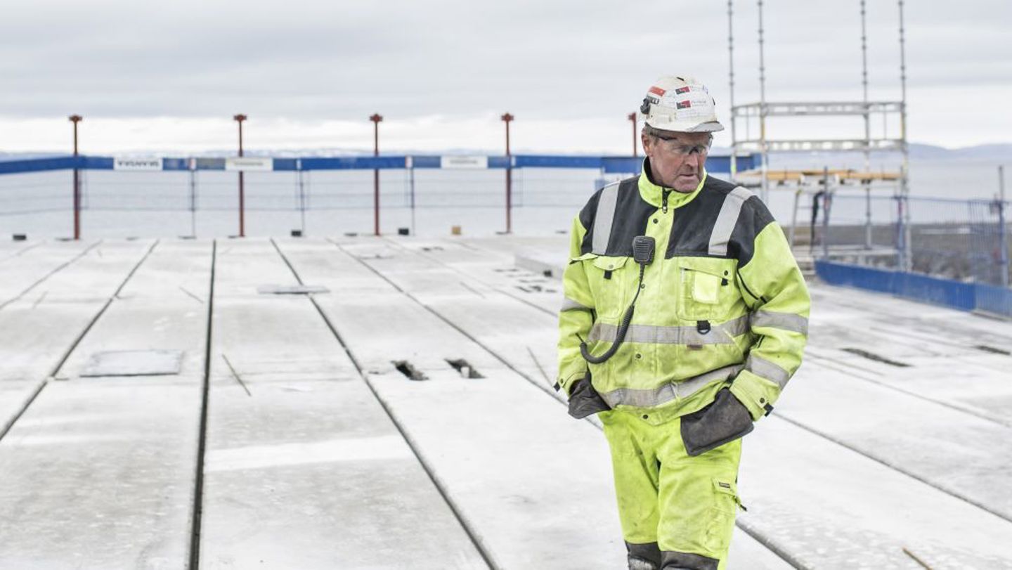 Bildet viser en mann som står på et snødekt tak på en byggeplass. 