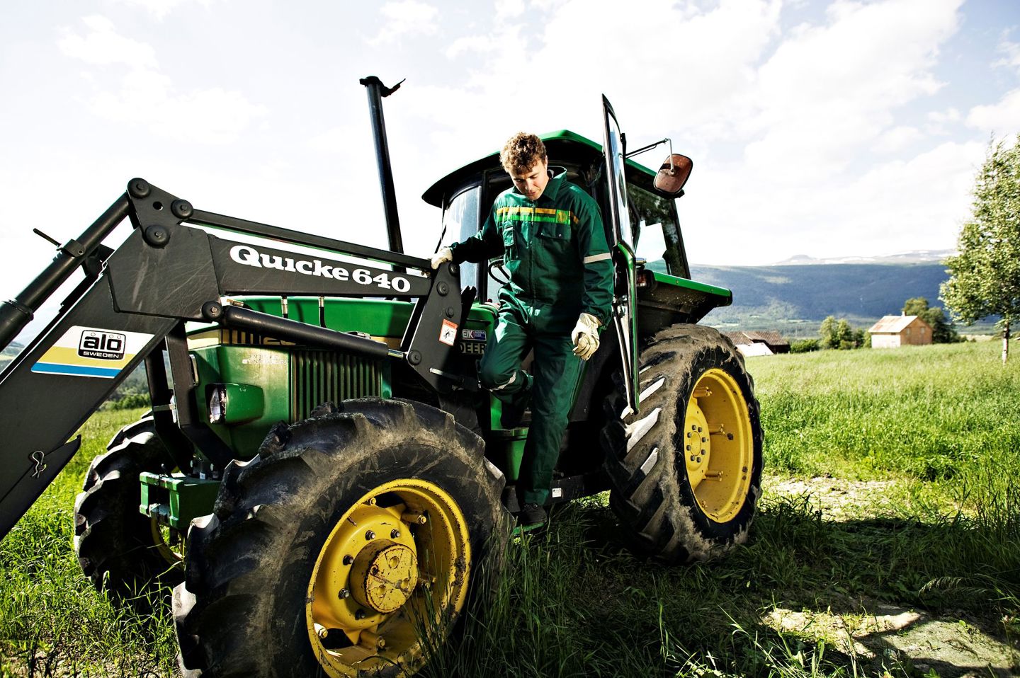 Fotografi av en mann i grønn kjeledress som stiger ut av en traktor på et jorde.