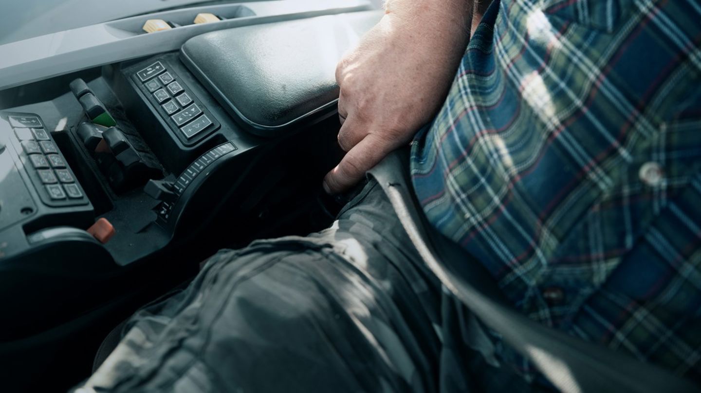Bildet er et utsnitt av en mann i en traktor som tar på seg setebeltet. 