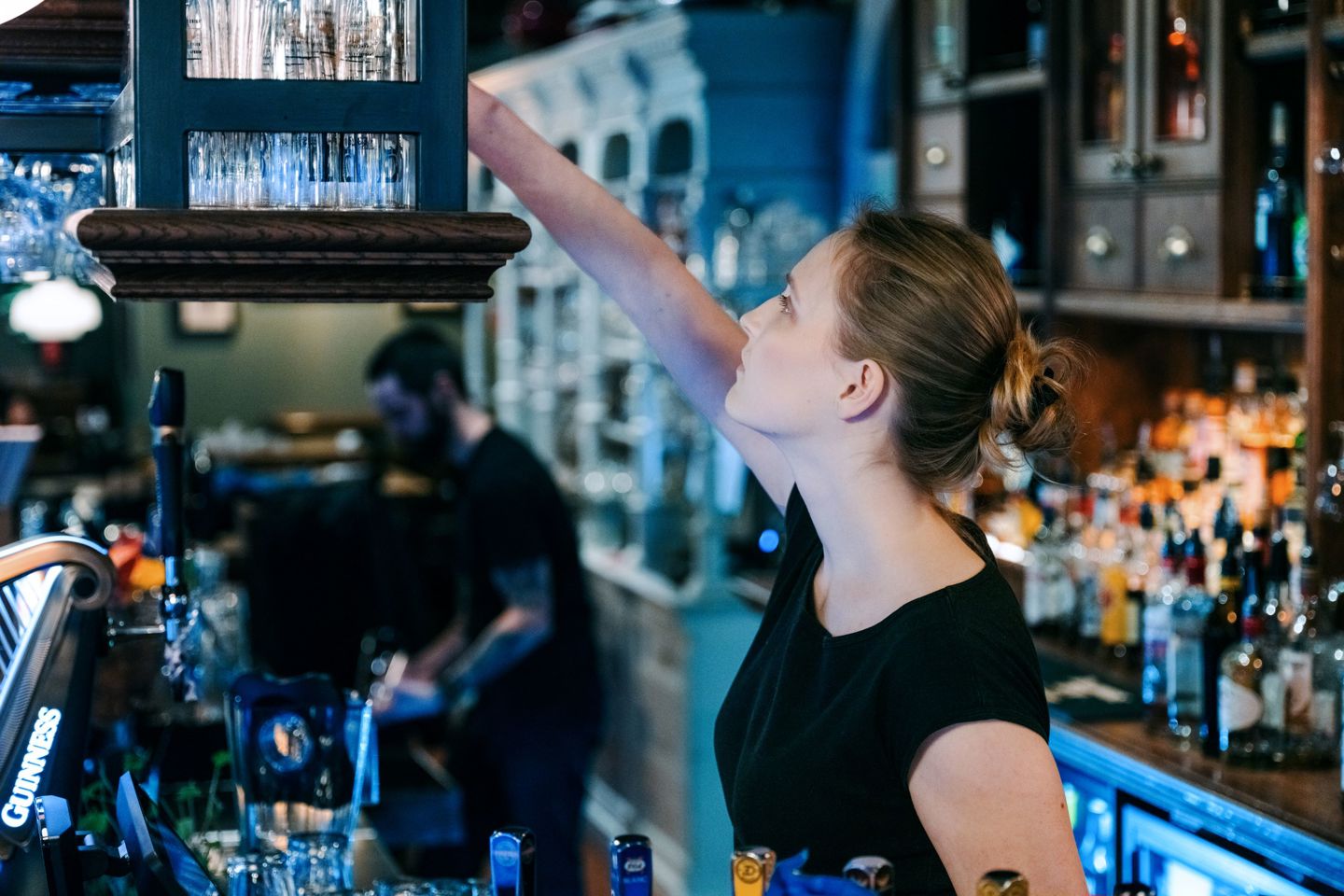 Bildet viser en kvinnelig servitør som jobber i en bar. 