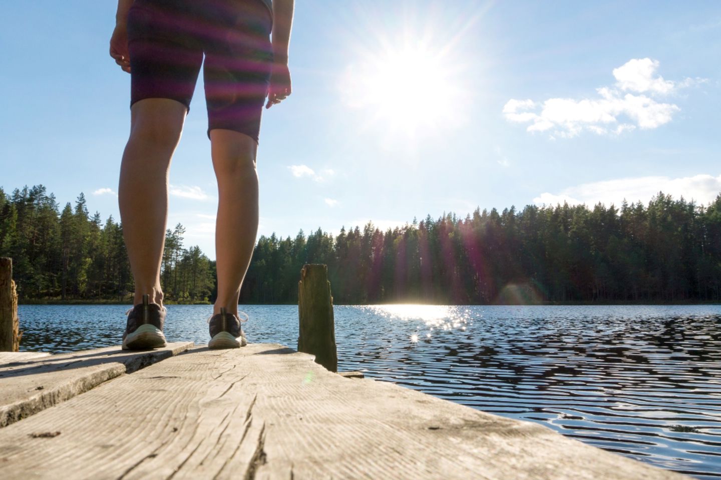 Bildet viser bein som står på ei brygge med skog og sol i bakgrunnen