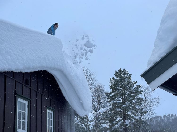 Bildet viser mann som måker snø av tak.