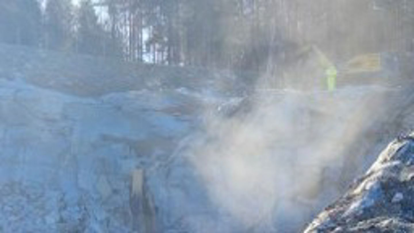 En sky av steinstøv ligger over et steinbrudd hvor en arbeider står ved en maskin 